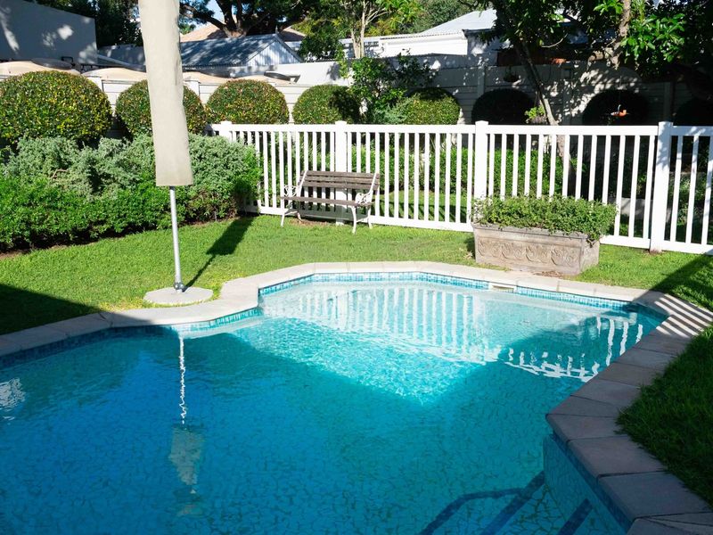 A well-maintained private swimming pool area featuring a clear pool, paved surround, and a white picket fence bordering a landscaped garden.