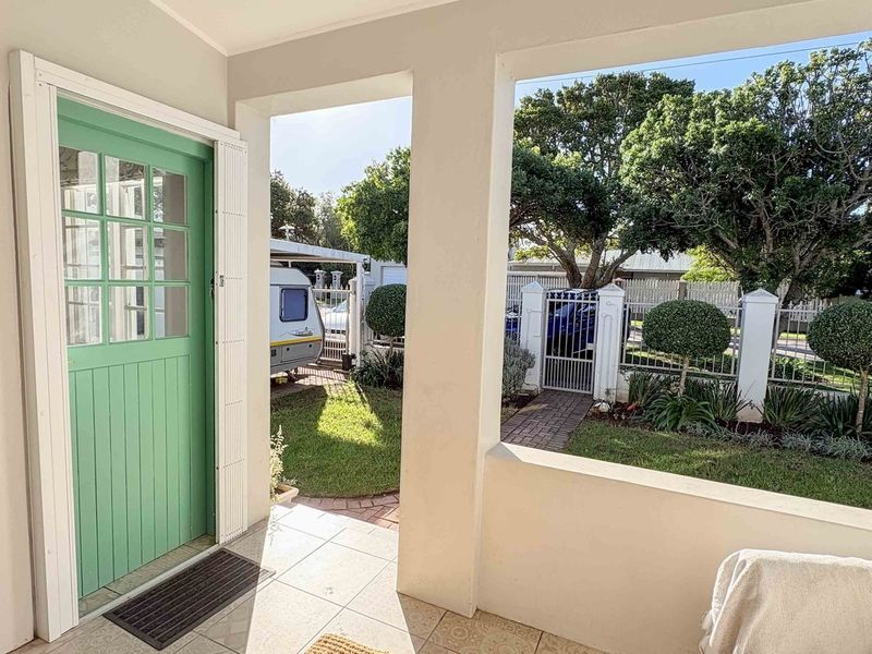 A covered patio area featuring tiled flooring and a distinctive green stable-style door, overlooking a well-maintained garden and secure perimeter fencing.