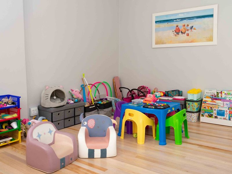 A bright and spacious room currently utilized as a children's play area, featuring light-toned hardwood flooring and neutral wall finishes.