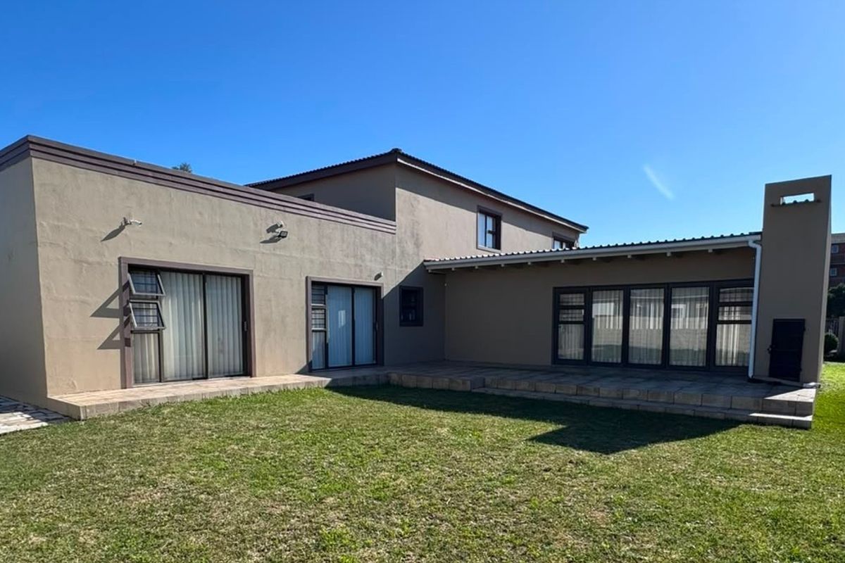 Rear view of the house featuring a paved patio area, built-in braai, and access to the garden through multiple sliding doors.
