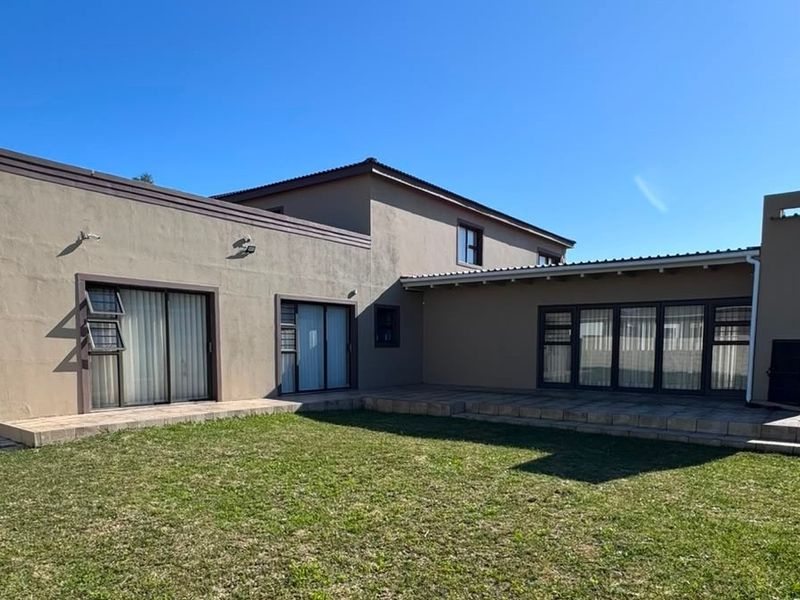 Rear view of the house featuring a paved patio area, built-in braai, and access to the garden through multiple sliding doors.