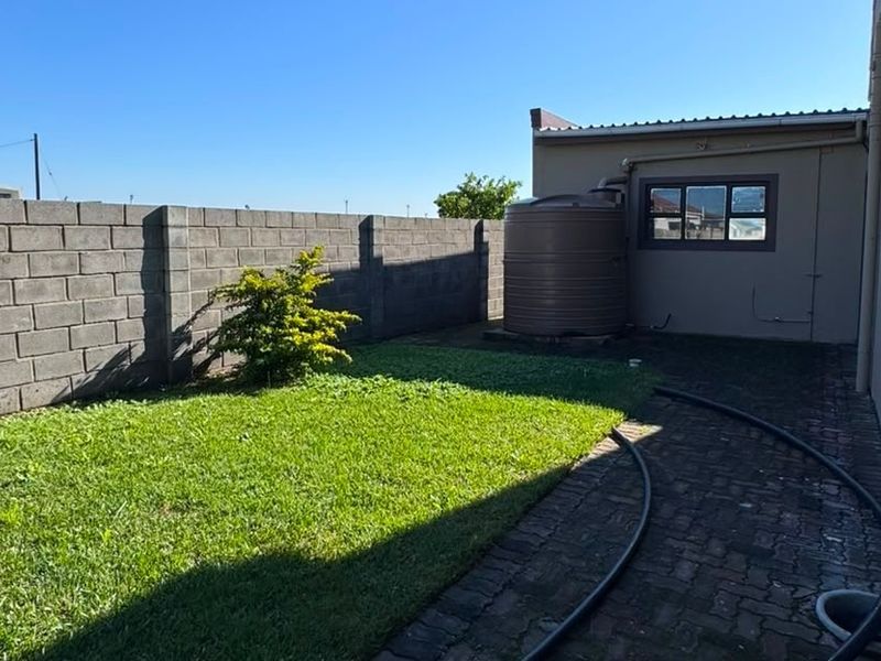 A private rear garden area featuring a paved walkway, a lawn, and a water storage tank enclosed by a concrete block boundary wall.