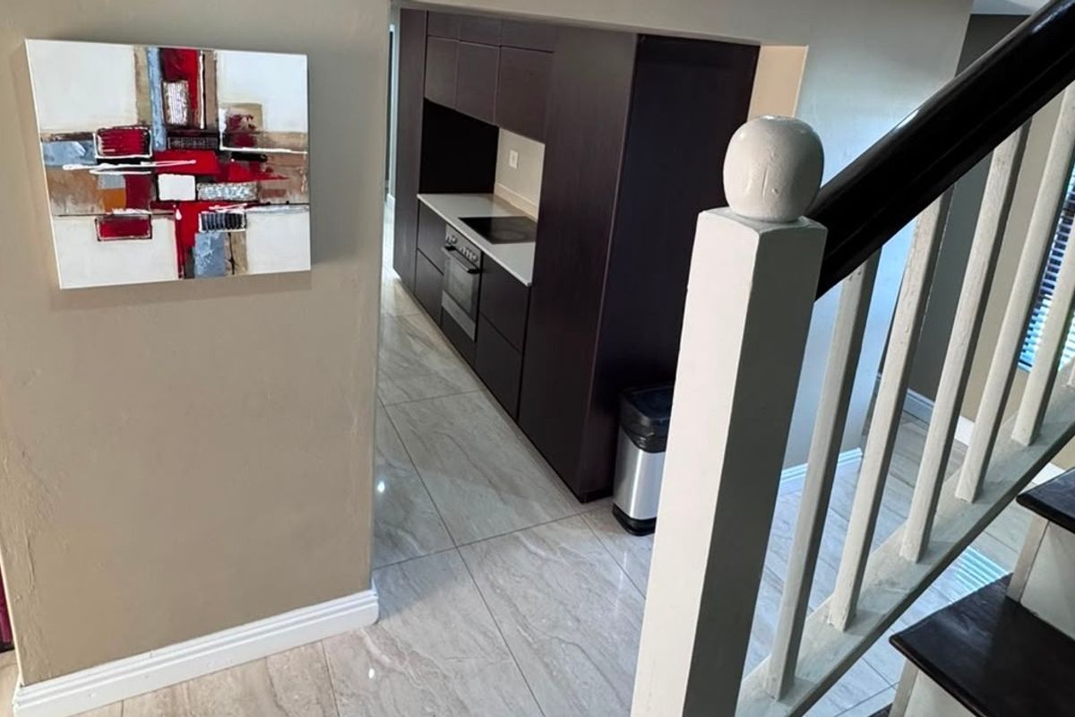 A modern kitchen area featuring dark built-in cabinetry, integrated oven and hob, and polished tiled flooring, viewed from the adjacent staircase.