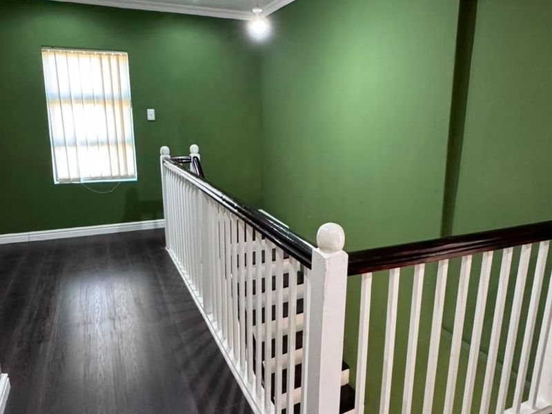 An empty upper-level landing area featuring dark laminate flooring, a white staircase balustrade, and green painted walls.
