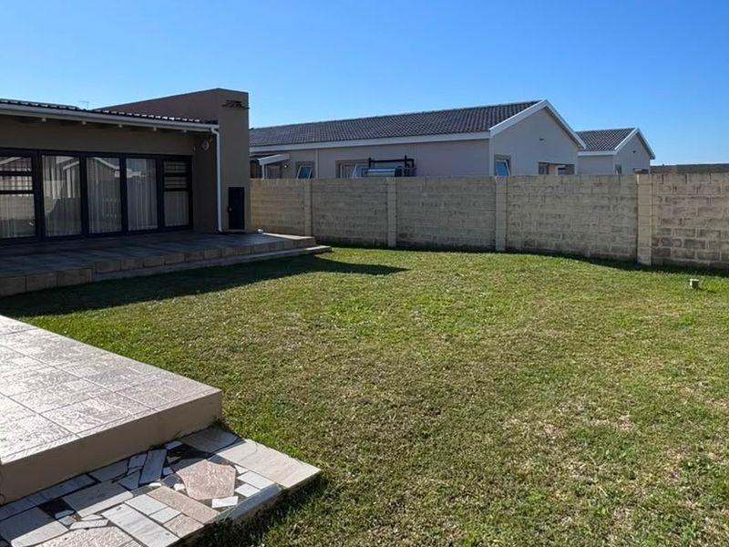 A spacious rear garden featuring a tiled patio area, lawn, and secure concrete block boundary walls, providing a private outdoor space.