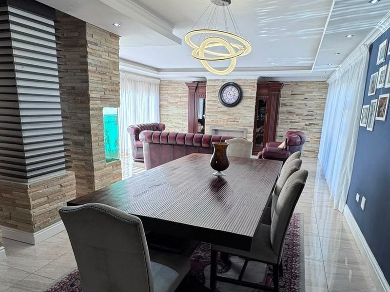 Spacious open-plan living and dining area featuring elegant stacked stone walls, recessed ceiling lighting, and polished tile flooring.