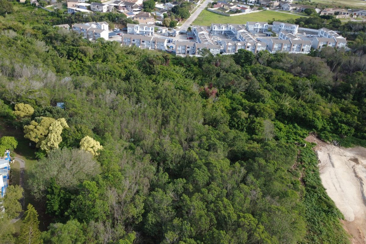 Aerial view of a vacant residential plot featuring dense vegetation and proximity to established residential housing developments.