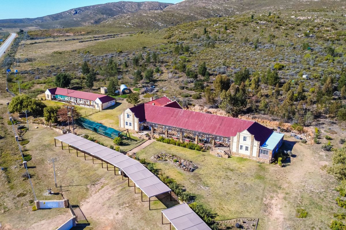 Aerial view of a rural guest house property featuring multiple buildings with red metal roofs, extensive grounds, and a long covered walkway.