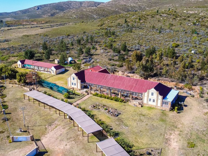 Aerial view of a rural guest house property featuring multiple buildings with red metal roofs, extensive grounds, and a long covered walkway.
