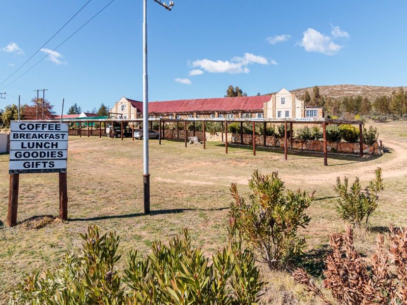 Front view of the guest house property featuring a long building with a corrugated metal roof, stone retaining wall, and extensive timber pergola structure.