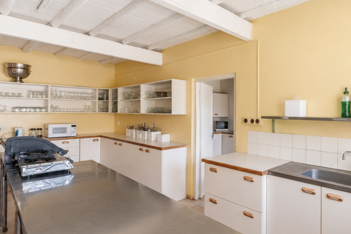 A functional kitchen featuring white cabinetry, stainless steel sink, tiled backsplash, and exposed beam ceilings, offering a practical layout for food preparation.