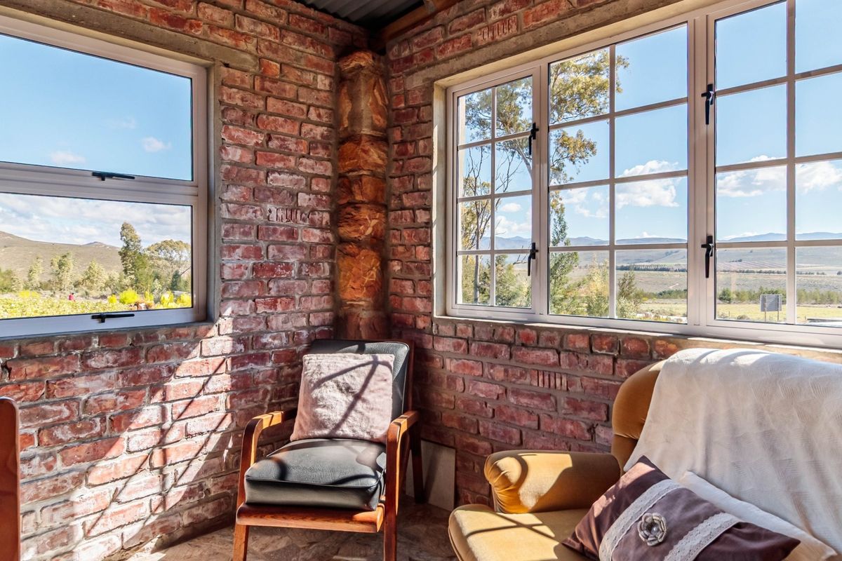 A cozy living area featuring rustic exposed brick walls, a stone corner pillar, and large windows offering scenic landscape views.