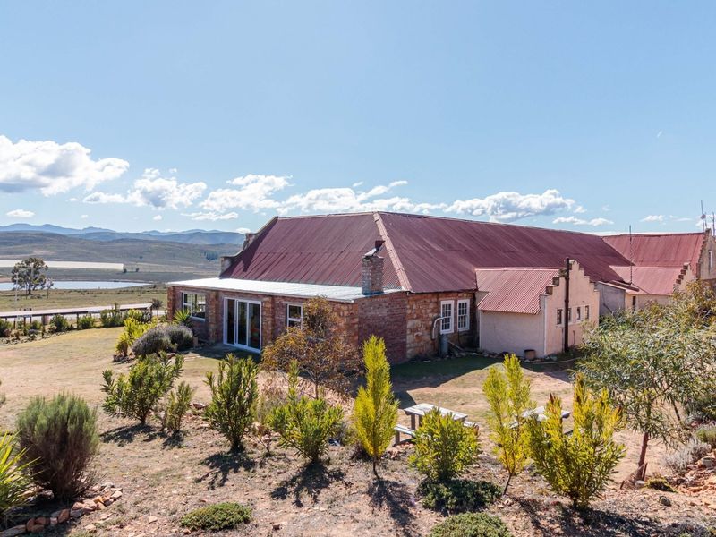 A rear view of a rustic stone guest house featuring a corrugated metal roof, large sliding glass doors, and expansive rural landscape views.