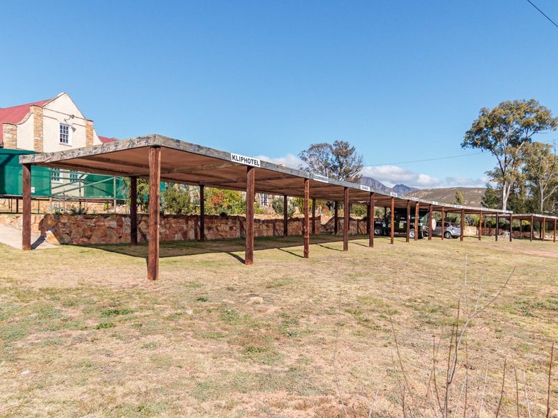 A long, covered outdoor parking structure with timber supports, situated on a grassy lot adjacent to the main guest house building.