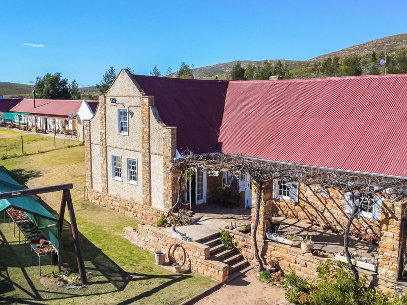 Aerial view of a rustic guest house featuring stone masonry walls, a red corrugated metal roof, and a covered patio area with a timber pergola.