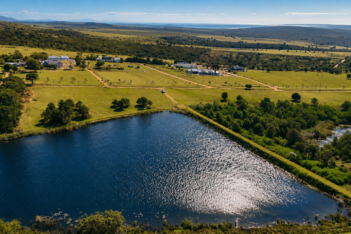 An aerial view of a large rural property featuring a prominent dam, expansive green pastures, and surrounding landscape with distant coastal views.