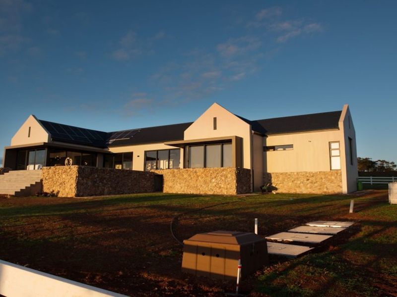 A modern residential property featuring stone cladding, large glass sliding doors, and solar panels, set against a clear sky.