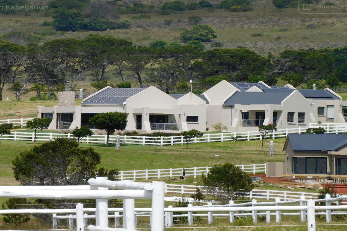 A wide-angle view of a residential property featuring multiple buildings with solar panels, stone accents, and extensive white post and rail fencing.