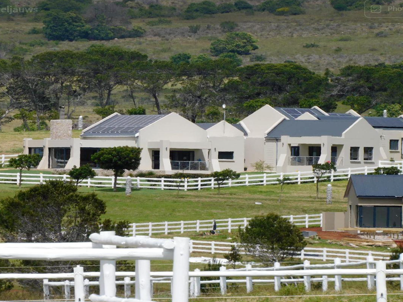 A wide-angle view of a residential property featuring multiple buildings with solar panels, stone accents, and extensive white post and rail fencing.
