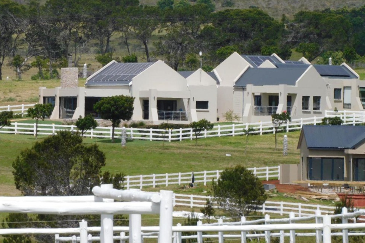 A view of a well-maintained residential property featuring multiple buildings, solar panels, stone accents, and extensive white post and rail fencing.
