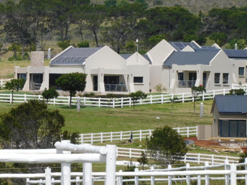 A view of a well-maintained residential property featuring multiple buildings, solar panels, stone accents, and extensive white post and rail fencing.