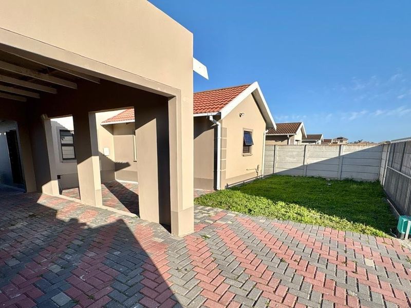 Front exterior view of the property featuring a paved driveway, covered carport, and a small lawn area enclosed by a precast concrete boundary wall.