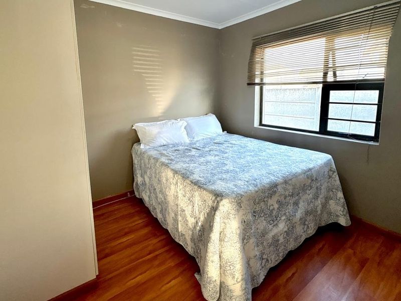 A functional bedroom featuring laminate flooring, a built-in wardrobe, and a window fitted with venetian blinds and security bars.