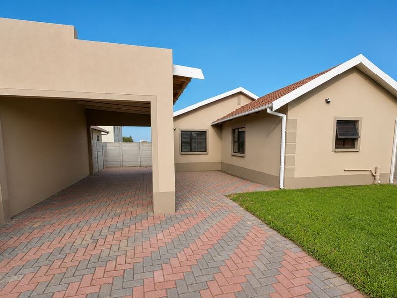 Rear view of the property featuring a paved driveway, covered carport, and a well-maintained lawn enclosed by a precast concrete boundary wall.