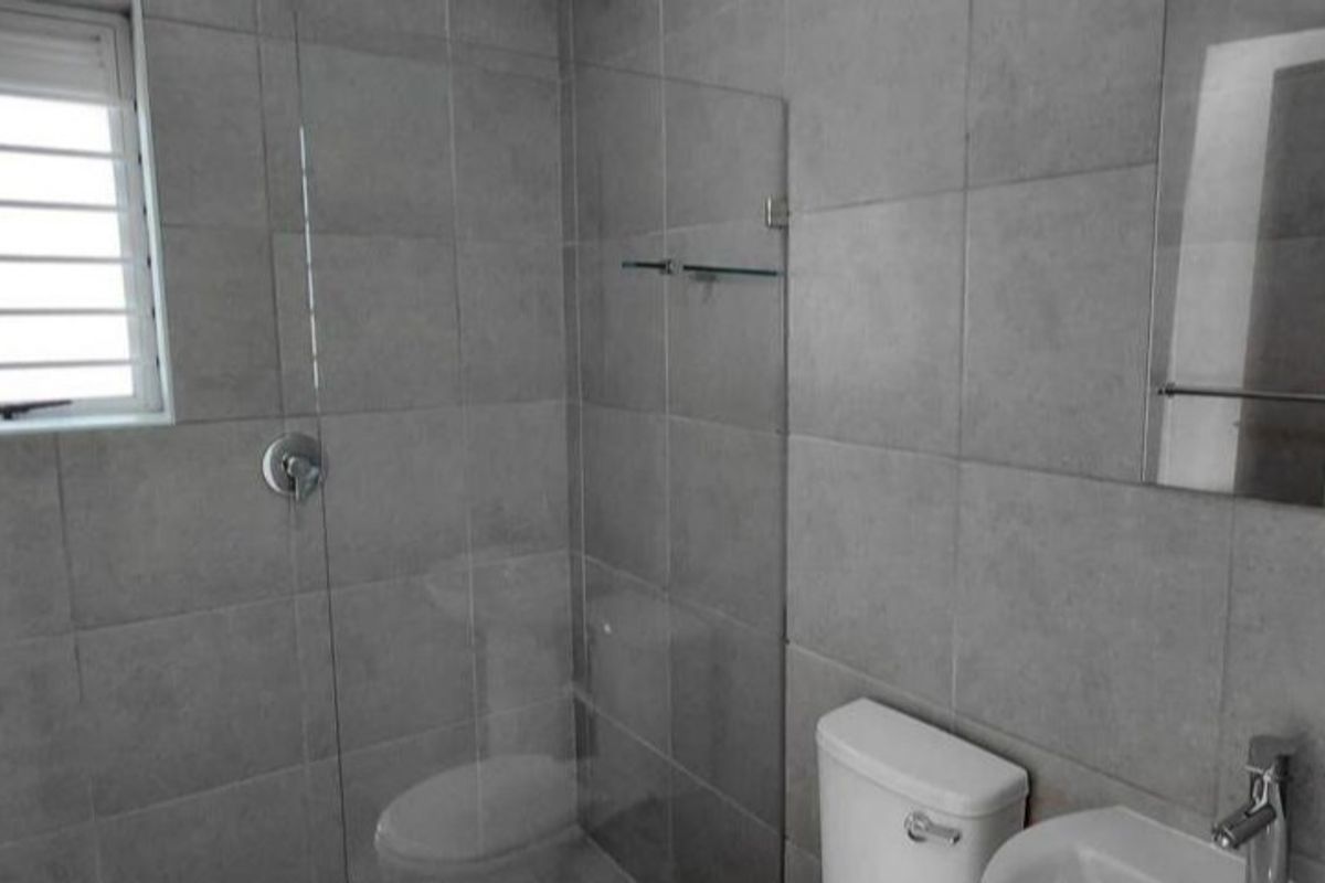 A modern bathroom featuring grey wall tiles, a glass shower screen, a pedestal basin, and a toilet.