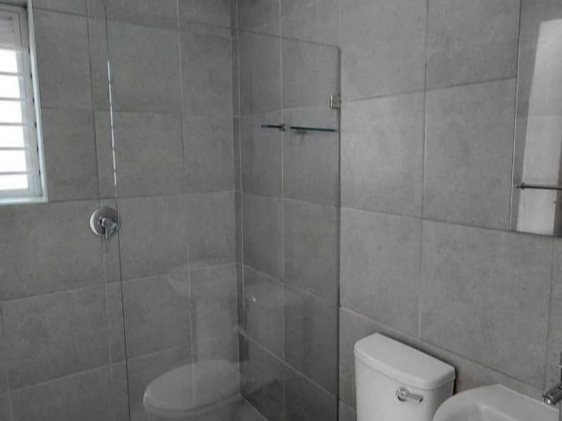 A modern bathroom featuring grey wall tiles, a glass shower screen, a pedestal basin, and a toilet.