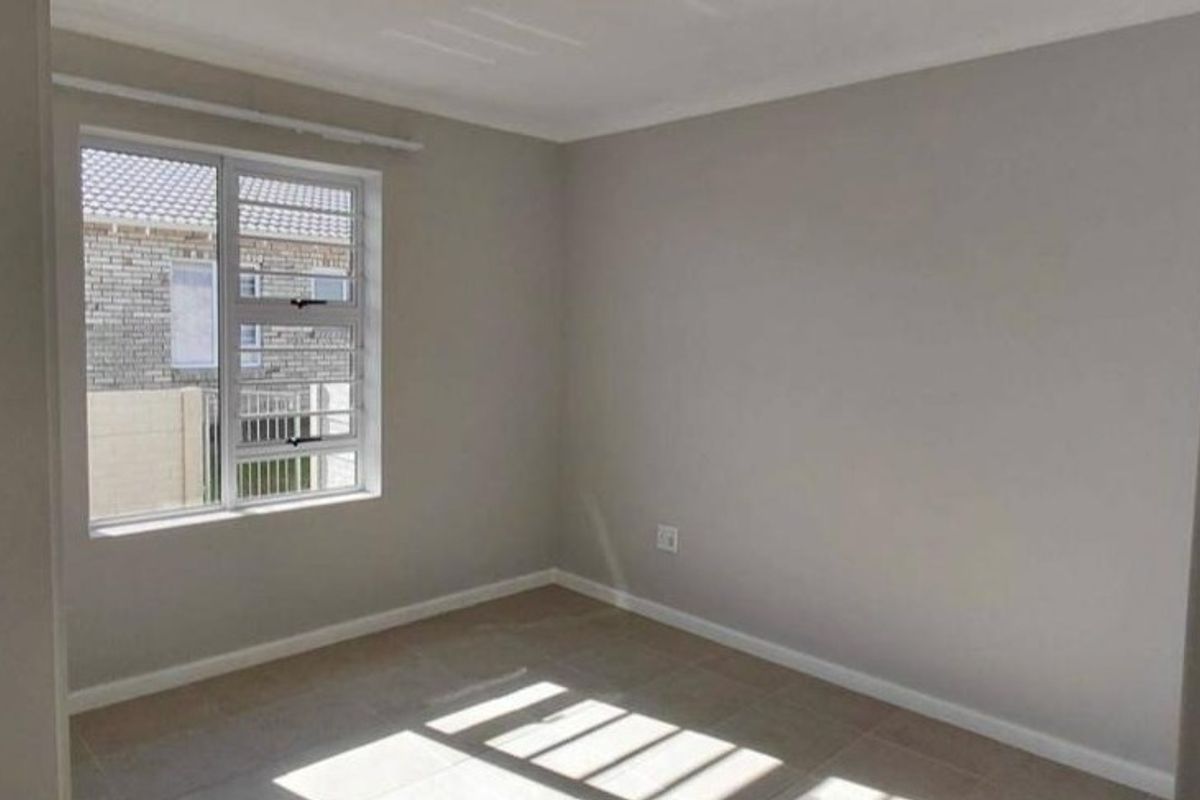 A clean, empty bedroom featuring neutral wall paint, tiled flooring, and an aluminium window with security bars, offering a bright and versatile living space.