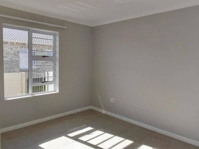 A clean, empty bedroom featuring neutral wall paint, tiled flooring, and an aluminium window with security bars, offering a bright and versatile living space.