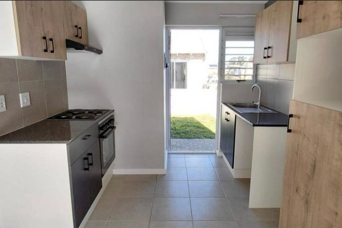 A modern, clean kitchen featuring built-in cabinetry, an electric hob, oven, and direct access to the rear garden area.