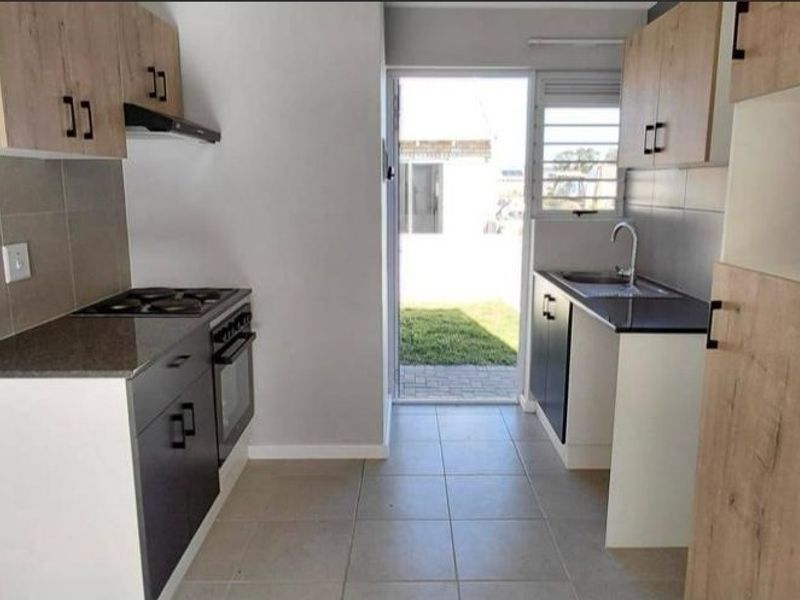 A modern, clean kitchen featuring built-in cabinetry, an electric hob, oven, and direct access to the rear garden area.