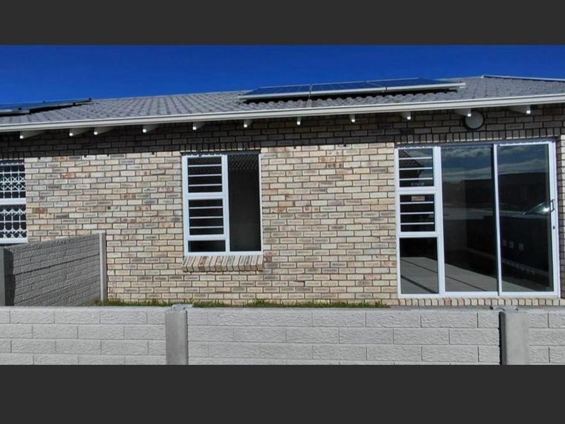 Rear view of the townhouse featuring a brick facade, tiled roof with solar panels, sliding glass door, and a secure precast concrete boundary wall.