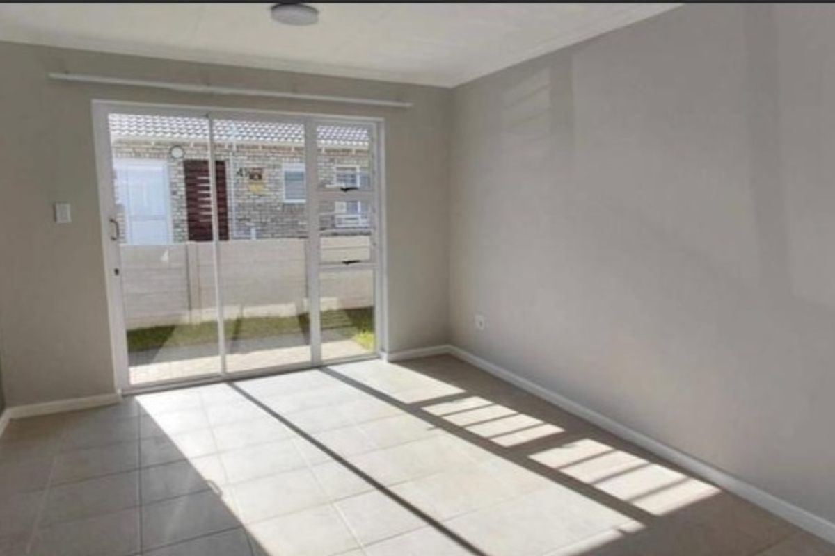 A bright, empty living area featuring neutral tiled flooring and a large sliding glass door providing access to the exterior.