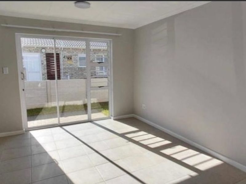 A bright, empty living area featuring neutral tiled flooring and a large sliding glass door providing access to the exterior.