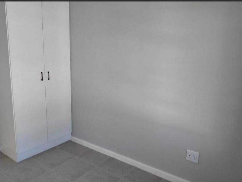 A clean, empty bedroom featuring neutral grey walls, tiled flooring, and a built-in wardrobe, providing a versatile space ready for personalization.