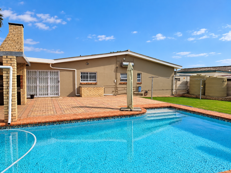 Rear garden area featuring a swimming pool, paved patio, built-in braai, and water storage tanks.