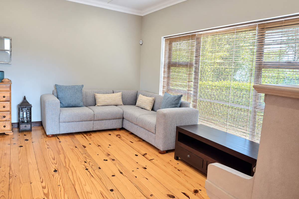 A bright living room featuring polished pine timber flooring, large windows with venetian blinds, and a neutral color palette with a fireplace surround.