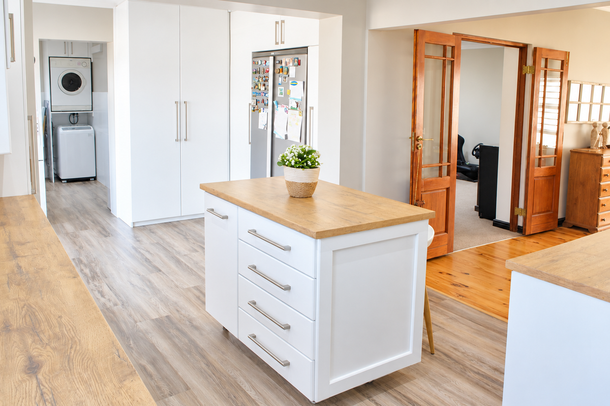 Modern kitchen featuring a central island with timber-look countertop, white cabinetry, and seamless transition to a laundry area and adjacent living space.