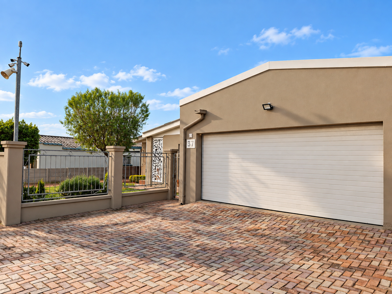 Front view of the property featuring a paved driveway, a modern sectional garage door, and secure perimeter fencing.