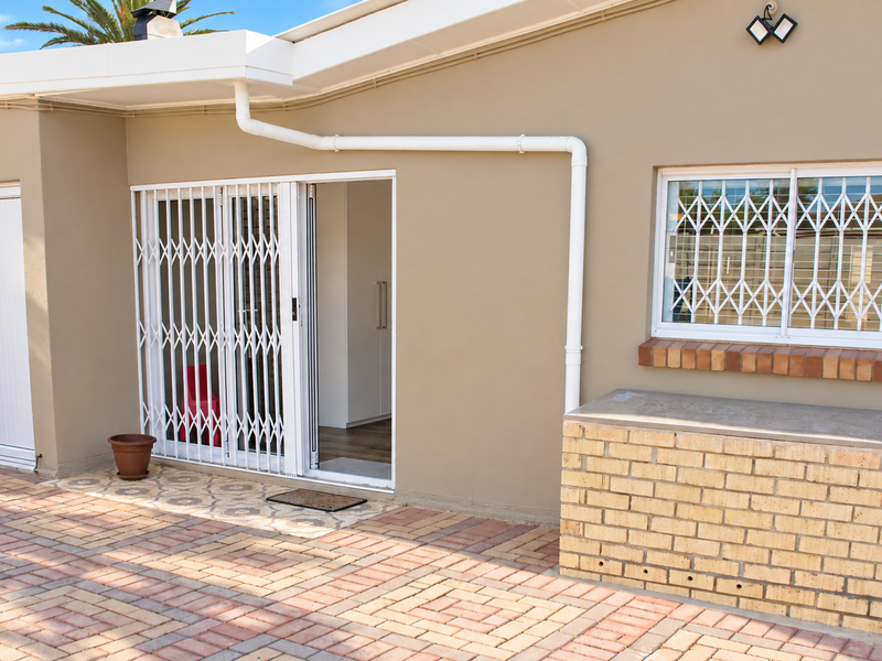 Rear exterior view featuring a paved patio area, brick built-in counter, sliding security gate, and window security bars.
