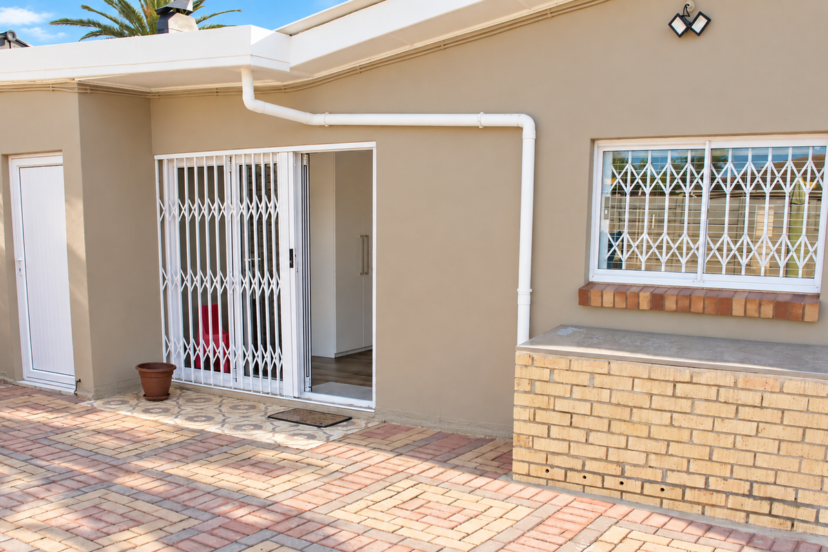 Rear exterior view featuring a paved patio area, brick built-in counter, sliding security gate, and window security bars.