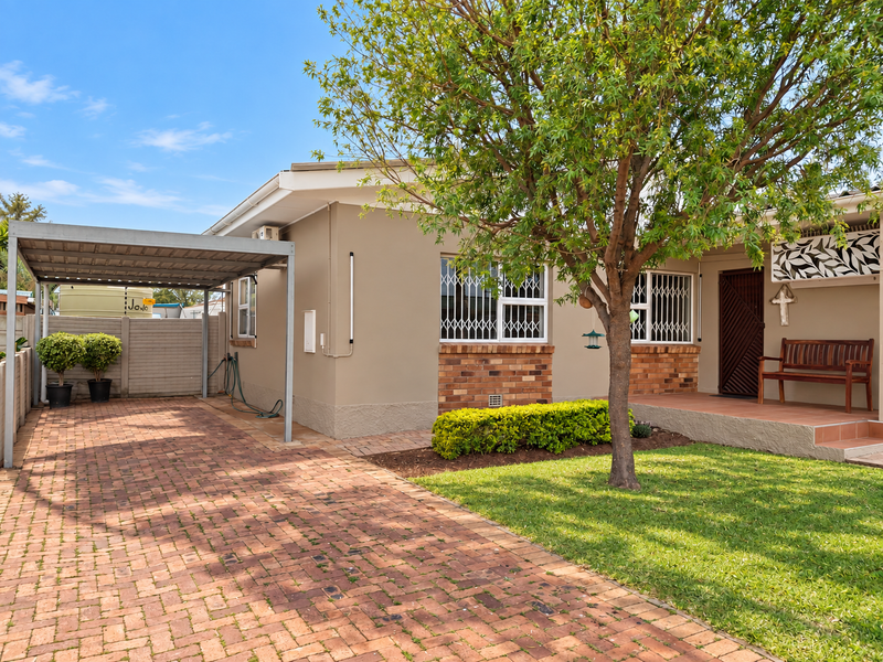 Front exterior view of the house featuring a brick paved driveway, a covered carport, and a well-maintained garden with a tiled entrance porch.