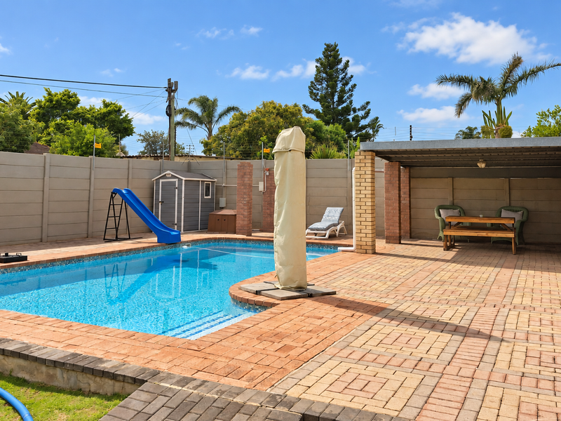 Outdoor entertainment area featuring a swimming pool, paved patio, and a built-in brick braai under a covered structure.
