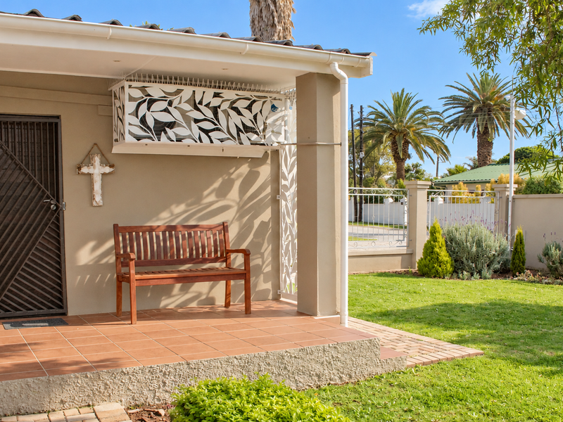 A well-maintained covered patio featuring tiled flooring, a secure entrance gate, and decorative screening, overlooking a landscaped garden area.