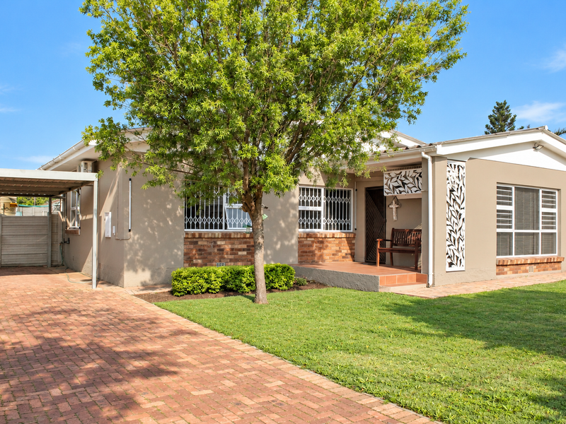 A well-maintained single-story home featuring a brick driveway, carport, landscaped front garden, and decorative security features on the facade.
