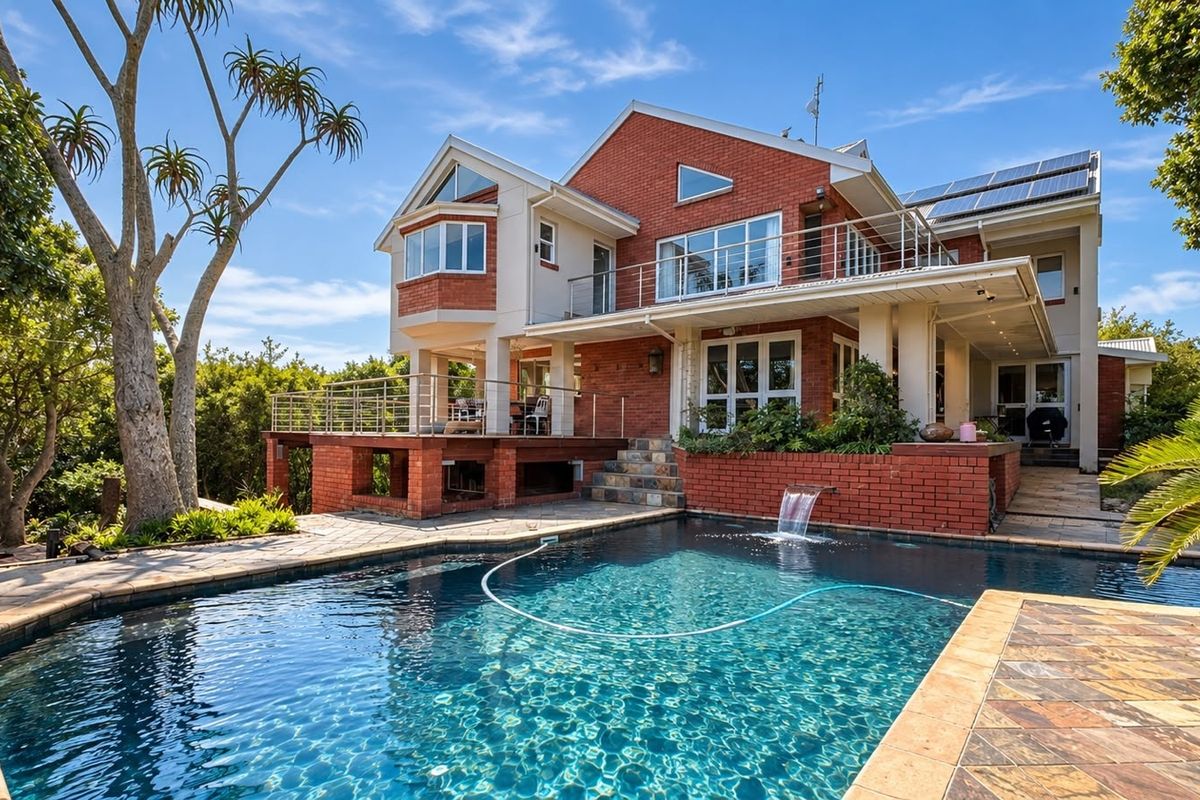 Rear view of a multi-level brick house featuring a swimming pool with a water feature, a raised deck, and an upper-level balcony.