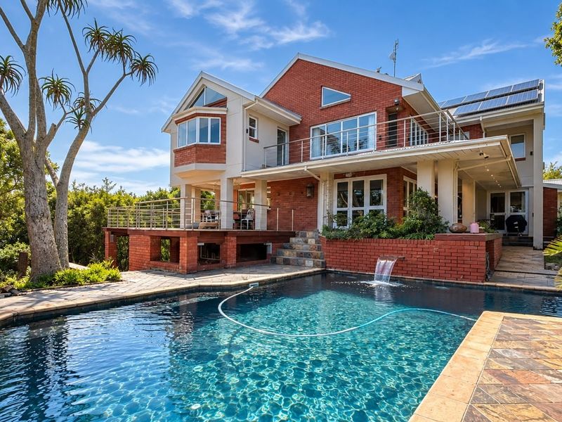 Rear view of a multi-level brick house featuring a swimming pool with a water feature, a raised deck, and an upper-level balcony.